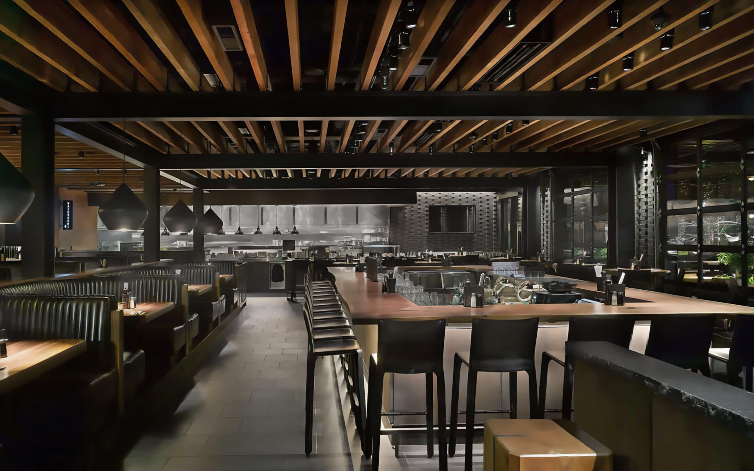 Restaurant interior with black booths, large high-top bar with stools, ambient lighting, and an open kitchen in the background.