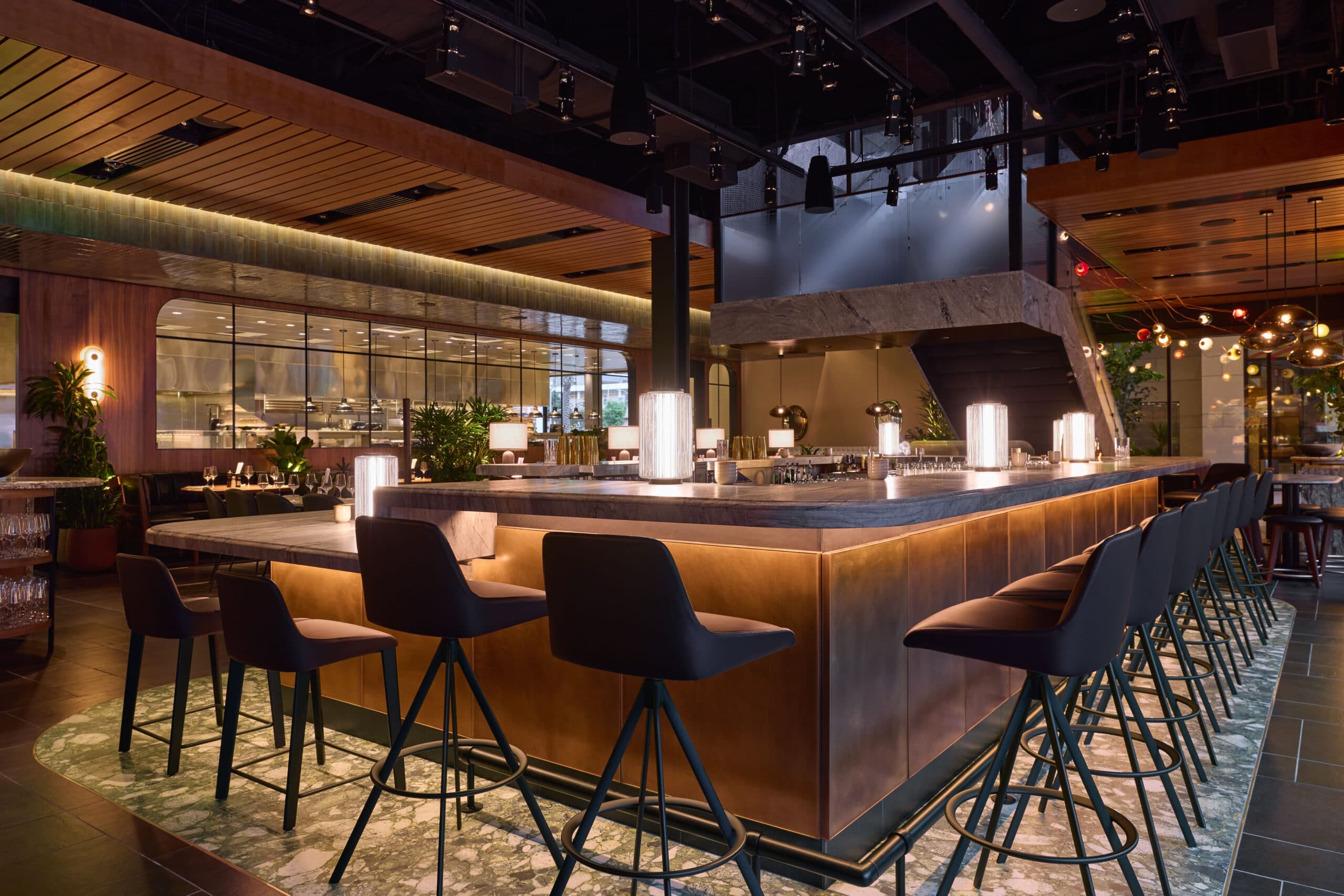 Restaurant interior with an under-lit bar, warm low lighting, and large glass windows revealing the open kitchen.